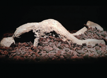 Plaster cast of a body on top of a bed of rocks, ankles shackled.